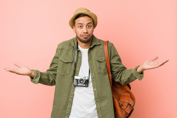 Young filipino traveler man doubting and shrugging shoulders in questioning gesture.