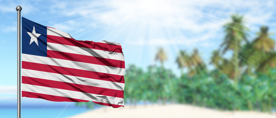 Waving Liberia flag in the sunny blue sky with summer beach background. Vacation theme, holiday concept.