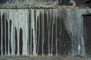 Old dark metal surface with drips of white paint