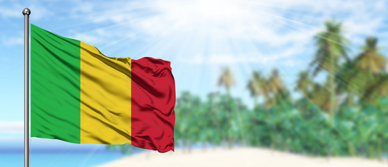 Waving Mali flag in the sunny blue sky with summer beach background. Vacation theme, holiday...
