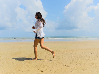Fototapeta na wymiar Woman runs on the beach against the background of sea of ​​clouds, in a light white shirt