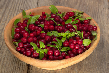 cowberries with green leaves in wooden cup on wooden background
