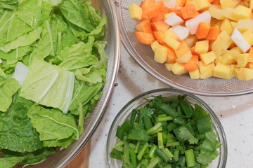 Glass bowl of cilantro, chard, potato, carrot and chives sliced. Ingredients to make a healthy dish 