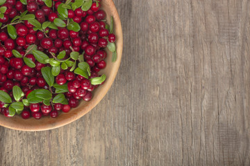 cowberries with green leaves in wooden cup on wooden background