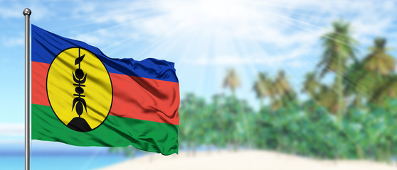 Waving New Caledonia flag in the sunny blue sky with summer beach background. Vacation theme, holiday concept.