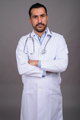 Handsome bearded Persian man doctor against gray background