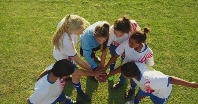 Female soccer team clasping hands together on soccer field.