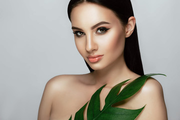 Beautiful woman face with perfect makeup and healthy skin with tropical leaf. beauty face care