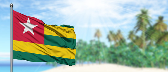 Waving Togo flag in the sunny blue sky with summer beach background. Vacation theme, holiday concept.
