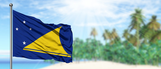 Waving Tokelau flag in the sunny blue sky with summer beach background. Vacation theme, holiday concept.