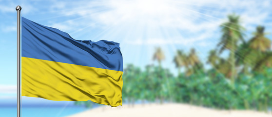 Waving Ukraine flag in the sunny blue sky with summer beach background. Vacation theme, holiday concept.