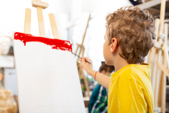 Curly blonde-haired boy coloring paper with red - Powered by Adobe