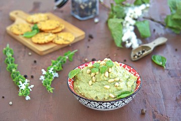 Green pea spread with almonds and basil on a brown concrete background. Decorated with pine nuts, served with crackers.