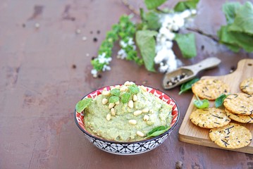 Green pea spread with almonds and basil on a brown concrete background. Decorated with pine nuts, served with crackers.