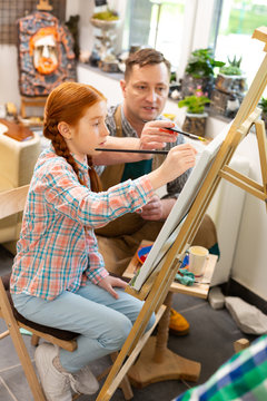 Pupil sitting near easel coloring picture with teacher