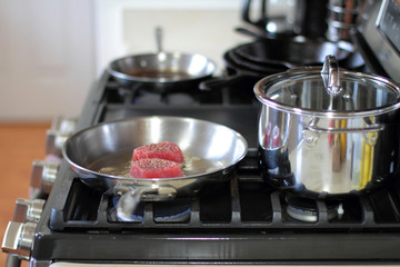 Ahi tuna steaks searing in a stainless steel pan on a gas stove.