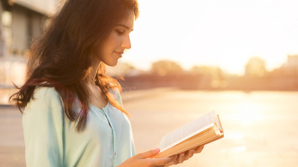 Student girl reading book outdoors, enjoying sunset