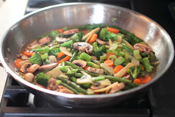 Stir fry vegetables cooking in a stainless steel pan.