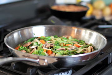 Stir fry vegetables cooking in a stainless steel pan.