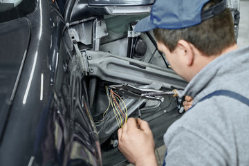 Back view of mechanic repairing wiring in auto door