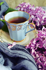 Tea in a blue Cup and fresh purple lilac flowers.