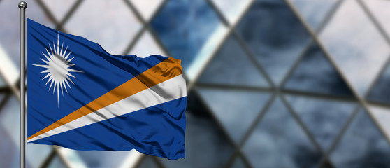 Marshall Islands flag waving in the wind against blurred modern building. Business concept. National cooperation theme.