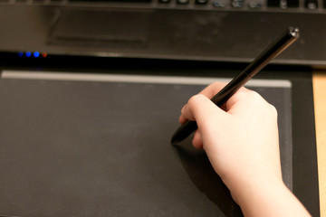 Female hand working on a black, graphic tablet. At the brown table