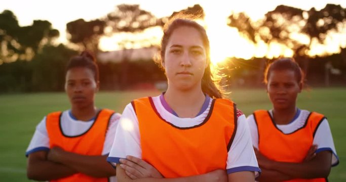 Female soccer players standing with arms crossed on soccer field.