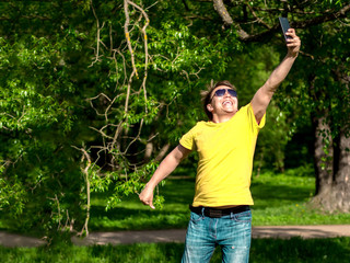 Handsome, sporty guy takes a selfie and jumping in the park. Young man in yellow t-shirt.