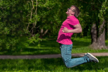 Handsome, sporty guy jumping in the park. Young man in pink t-shirt.