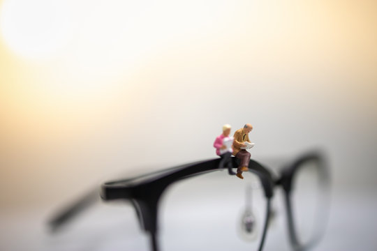 Education and Business Concept. Close up of businessman miniature figures sitting and reading book on reading glasses with copy space for text.