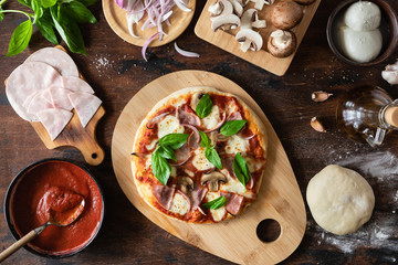 Top view of homemade Pizza with background of raw dough, ingredients and spices, ham and mushrooms on wooden background.