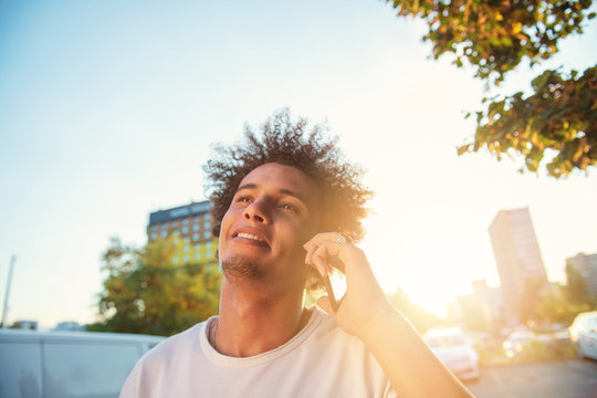 Happy Smiling Urban Hipster Young Man Using Smart Phone. African American Teenager Holding Mobile Smartphone On Sunset With Lens Flare