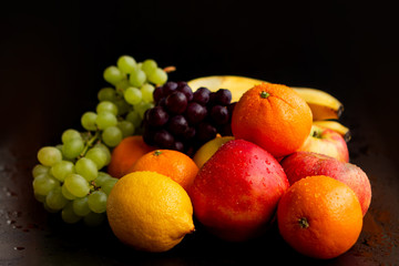 Naklejka na ściany i meble Beautiful juicy fruits on a black wet background: apples, grapes, oranges, bananas, copy space, close-up