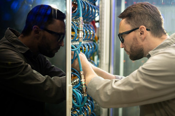 Side view of concentrated young server repairman in glasses standing in server room and connecting...