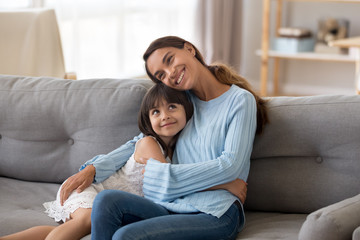Cute happy daughter hug young mommy sitting on couch