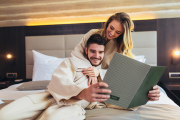 Couple in hotel room reading room service menu together in bed