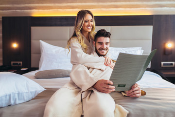 Couple in hotel room reading room service menu together in bed