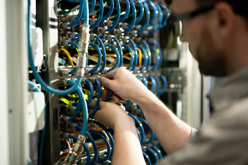 Close-up of busy server support specialist inserting cables into hubs and examining connectivity...