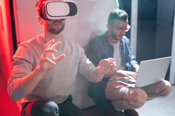 Arabian IT engineer typing on laptop while transferring data to colleague in VR goggles in data center