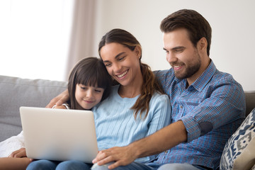 Happy young parents with little daughter watch cartoon on laptop