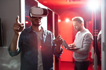 Serious hipster young middle-eastern IT scientist pointing with finger and using virtual reality...