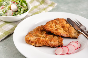 Fried pork chop in breadcrumbs served with radishes and lettuce.