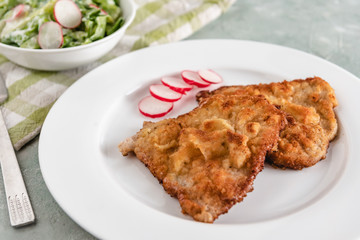 Fried pork chop in breadcrumbs served with radishes and lettuce.