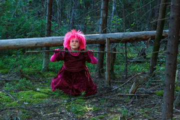 A young witch in purple clothes in the forest conjures a dry branch of a tree.