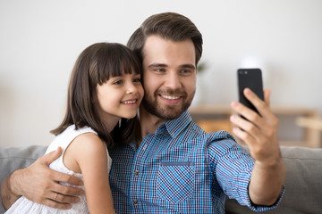 Fototapeta premium Smiling young dad and little daughter making selfie on smartphone