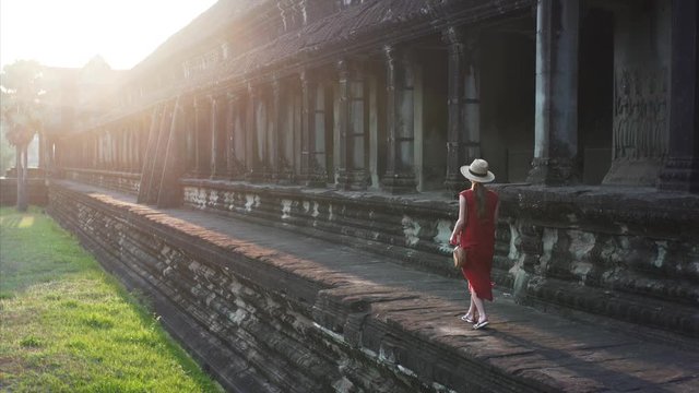 Slider. Woman in red dress is exploring the Angkor Wat temple lit by sunlight and taking photos on her smartphone. It was built in 12th century by khmer civilization. Cambodia