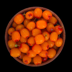 heap of sea buckthorn in wooden plate isolated on black background. top view