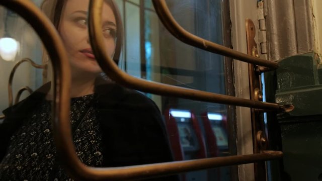 Attractive middle aged brunette woman in a black coat behind a glass vintage door. Warm, muffled light, twilight.