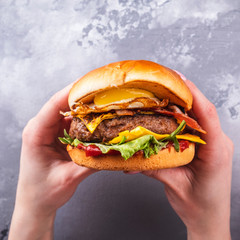 Female hands holding tasty beef burgers with fried egg and bacon. Top view. Closeup